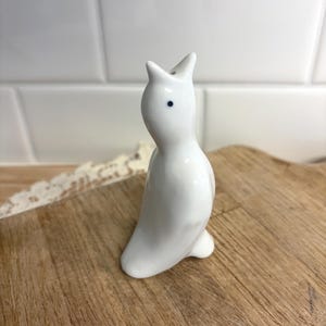 May include: A white ceramic mug with a black handle and the text "But First, Coffee" in a bold, black font. The mug is set against a neutral background, highlighting its simple design.