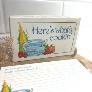 May include: A white recipe card box and a matching lined recipe card. Both feature a blue pitcher illustration, corn, strawberries, grapes, and a peach. The text reads Here's what's cookin, Serves, and Recipe from the kitchen of in blue font.