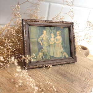 May include: A rectangular picture frame with a dark brown, textured finish containing a vintage-style print. The artwork depicts three children standing together in formal attire, accompanied by two small dogs positioned at their feet.