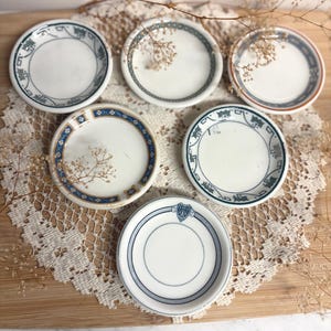 May include: A collection of six small, round ceramic dishes featuring various decorative borders in shades of blue, white, and orange. Each dish has a smooth, concave center and distinct patterns along the rim, including geometric shapes and floral motifs.