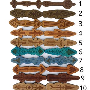 Puede incluir: Una colección de diez adornos de madera en forma de flecha con varios diseños y colores. Las flechas varían de marrón oscuro a marrón claro, con algunos detalles en turquesa y azul. Cada flecha tiene un patrón tallado único.