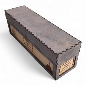 以下が含まれることがあります： グレー仕上げと装飾的なデザインの長方形の木製ボックス。ボックスは、前面と側面にレーザーカットのデザインが施されており、「Against the Shadow」の文字がラベルに表示されています。ボックスは、連動するジョイントで設計されています。