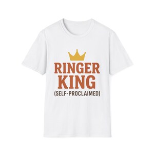 May include: White t-shirt with the text "RINGER KING (SELF-PROCLAIMED)" in brown letters and a gold crown graphic above the text. The shirt has short sleeves and a crew neck.