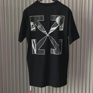 Puede incluir: Camiseta negra con un diseño gráfico blanco en la espalda. El diseño presenta cuatro flechas blancas que forman una X, con imágenes en blanco y negro dentro de las flechas. La camiseta está colgada de una percha negra.