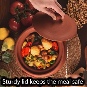 Puede incluir: Una olla de cocina de terracota con tapa, llena de verduras y alimentos cocinados. La olla está sobre una estera tejida, con tomates y limones en el fondo. El texto "Sturdy lid keeps the meal safe" está en la parte inferior.