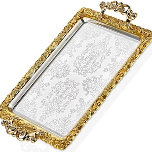 Può includere: Un vassoio rettangolare con interno argentato e cornice dorata ornata. Il vassoio presenta manici decorativi e un motivo floreale dettagliato sulla superficie argentata. La cornice dorata ha un design in rilievo intricato.