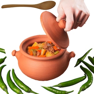 May include: A terracotta cooking pot with a lid, filled with a stew of vegetables and meat. A wooden spoon rests above the pot. Green chili peppers surround the pot, suggesting a spicy dish.