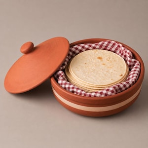 May include: A round terracotta tortilla warmer with a matching lid, featuring a light-colored band around the center. Inside, a stack of round, beige flour tortillas rests on a red and white gingham cloth liner, providing a rustic presentation.