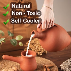 Può includere: Una brocca di terracotta versa del liquido in una tazza abbinata. La brocca e la tazza sono di un caldo colore marrone-rossastro. Il testo "Natural, Non-Toxic, Self Cooler" è visibile sullo sfondo.