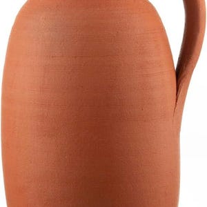 Può includere: Una brocca color terracotta con coperchio e manico. La brocca ha un corpo arrotondato, un beccuccio e un piccolo coperchio rotondo. Il manico è curvo e attaccato al lato. La superficie ha una consistenza leggermente ruvida.