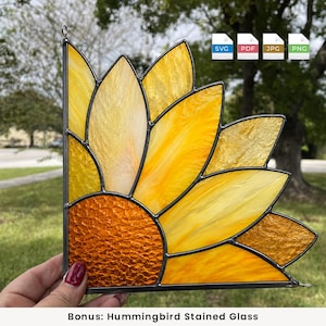 Può includere: Un acchiappasole in vetro colorato a forma di quarto di girasole, con vetro ambrato testurizzato al centro e varie tonalità di vetro giallo per i petali, il tutto unito da saldature in metallo scuro con un piccolo gancio per appenderlo.