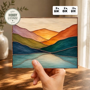 May include: A stained glass panel depicting a landscape with layered mountains in shades of orange, green, blue, and purple. The artwork is framed with a copper border and held by a hand. The panel has a "HOBBY LICENSE" sticker.