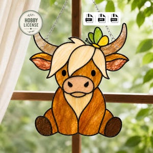 May include: A stained glass window decoration featuring a cartoon Highland cow with a butterfly. The cow is primarily brown and tan with a light-colored fringe and horns. The butterfly is yellow and green. The window art hangs from a silver chain.