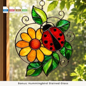 May include: A stained glass suncatcher featuring a red ladybug with black spots perched on a yellow flower with an orange center, surrounded by green leaves and dark metal wire accents. The design includes a hanging loop at the top.