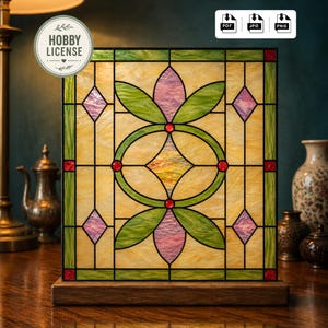 May include: A square stained glass panel with a floral design, featuring green leaves, pink petals, and red accents. The panel is set in a wooden base. The words "HOBBY LICENSE" are in a circular badge.