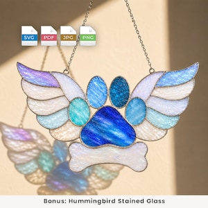 May include: A stained glass suncatcher featuring a central blue paw print shape with a white bone at the base and two expansive wings extending from the sides. The wings are composed of iridescent white, light blue, and purple glass segments.