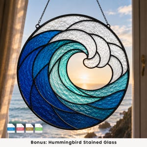 May include: A circular stained glass suncatcher featuring a stylized ocean wave design. The piece uses textured glass in shades of deep blue, turquoise, and white, held together by black metal lead lines. It hangs from a thin metal chain.