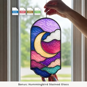 Op de afbeelding: Een boogvormige glas-in-lood zonnevanger met een gele maansikkel tegen een nachtelijke hemel van getextureerde paarse, blauwe en roze wolken. Het stuk is omlijst in donker metaal en bevat een ketting, wat een levendig hemels ontwerp laat zien.