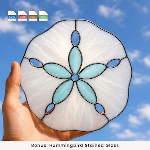 May include: A sand dollar stained glass suncatcher featuring white textured glass with five central light blue petal-shaped glass segments, all held together by dark metal solder lines. The design includes five small oval cutouts along the edge.