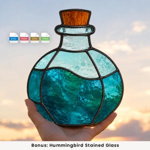 Könnte beinhalten: Eine Buntglas-Zaubertrankflasche mit einem strukturierten, hellblauen oberen Teil und einem tiefen, leuchtend türkisfarbenen unteren Teil, verbunden durch dunkle Metalllötstellen. Die Flasche hat einen strukturierten, bernsteinfarbenen Glasstopfen.