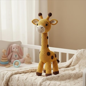 Op de afbeelding: Een handgemaakte gehaakte giraf speelgoed in geel met bruine vlekken en accenten. De giraf heeft een lange nek, kleine oren en een schattig gezicht. Het staat op een wit babybedje.