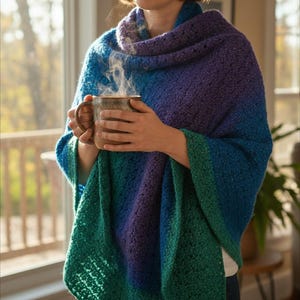 Könnte beinhalten: Ein gehäkelter Schal in Blau, Lila und Grün. Der Schal ist über den Schultern drapiert. Eine Person hält eine braune Tasse, aus der Dampf aufsteigt. Der Schal hat einen Farbverlauf, der von Blau über Lila nach Grün verläuft.