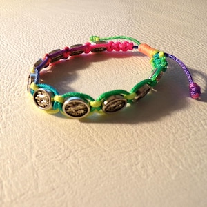 Puede incluir: Una colorida pulsera de la amistad con cierre de nudo corredizo. La pulsera presenta una serie de abalorios circulares plateados y est&aacute; hecha con una combinaci&oacute;n de cordones verdes, amarillos, azules, rosas y morados.