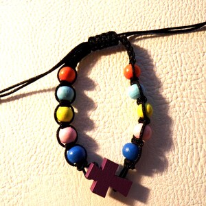 May include: A colorful beaded bracelet with a black cord. The bracelet features a series of round, wooden beads in various colors, including red, blue, yellow, and pink. A purple cross is attached to the bracelet.