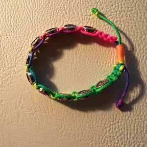 Puede incluir: Una colorida pulsera de macram&eacute; con cierre de nudo corredizo. La pulsera presenta un arco&iacute;ris de colores, incluyendo rosa, verde, amarillo y morado. Tiene abalorios circulares plateados. La pulsera mide aproximadamente 18 cm de largo.