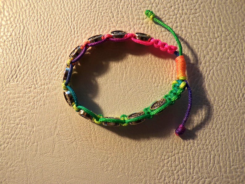Puede incluir: Una colorida pulsera de macram&eacute; con cierre de nudo corredizo. La pulsera presenta un arco&iacute;ris de colores, incluyendo rosa, verde, amarillo y morado. Tiene abalorios circulares plateados. La pulsera mide aproximadamente 18 cm de largo.