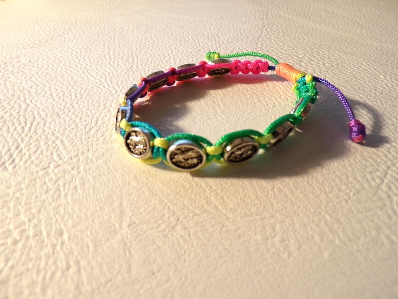 Puede incluir: Una colorida pulsera de la amistad con cierre de nudo corredizo. La pulsera presenta una serie de abalorios circulares plateados y est&aacute; hecha con una combinaci&oacute;n de cordones verdes, amarillos, azules, rosas y morados.