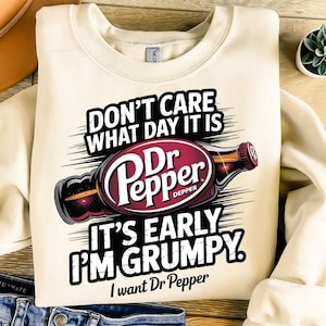 May include: Cream-colored sweatshirt with the text "DON'T CARE WHAT DAY IT IS, IT'S EARLY I'M GRUMPY. I want Dr Pepper." A graphic of a Dr Pepper bottle is in the center. The sweatshirt is made of a soft material.