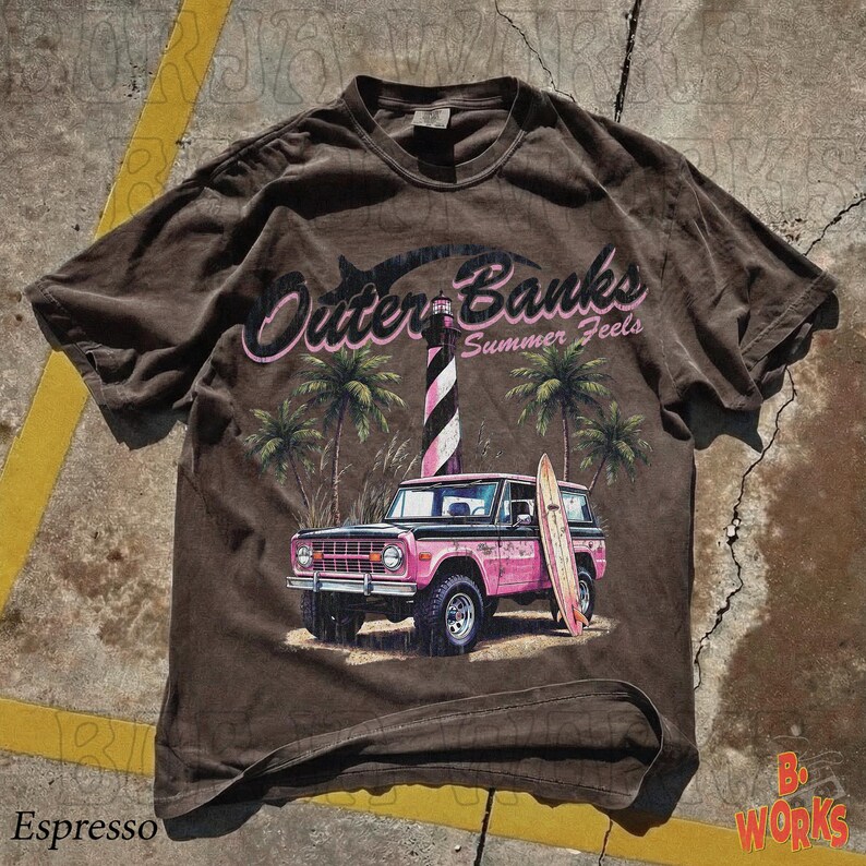 May include: Espresso-colored t-shirt featuring a graphic of a pink vintage SUV with a surfboard, palm trees, and a lighthouse. The text "Outer Banks Summer Feels" is arched above the scene. The shirt has a vintage, worn look.