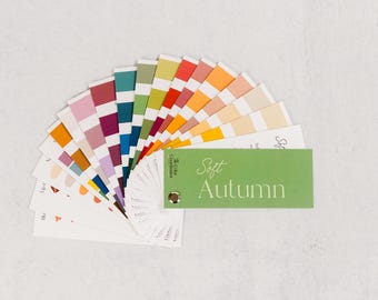 May include: A color palette fan featuring a variety of colors, including shades of pink, blue, green, and orange. A green card with the text "Soft Autumn" is attached. The palette is arranged in a semi-circle on a white surface.