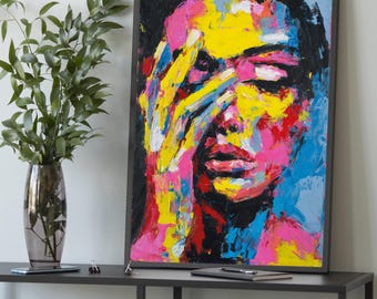 Puede incluir: Pintura de retrato abstracto con marco negro. La obra presenta un rostro con una mano cubriendo los ojos. La pintura utiliza pinceladas audaces y colores vibrantes, incluyendo amarillo, rosa, rojo y azul. La obra se exhibe sobre una mesa gris oscuro.
