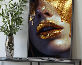 Peut inclure: Gros plan d'une impression d'art encadrée représentant un visage partiellement recouvert de peinture dorée. Les lèvres et la peau sont peintes en or, avec des coulures de peinture. L'œuvre est exposée sur une table grise foncée.