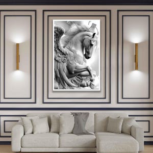 May include: A black and white framed print of a winged horse, Pegasus, in a dynamic pose. The artwork is displayed on a wall with gold sconces and a light-colored sofa. The room has a modern, elegant aesthetic.