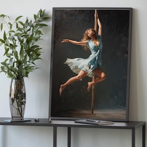 Op de afbeelding: Een ingelijste kunstdruk toont een vrouw in een zwierige blauwe jurk in de lucht, sierlijk geposeerd op een paal. Het kunstwerk is geplaatst tegen een donkere, getextureerde achtergrond, met de vorm van de vrouw verlicht. De lijst is zwart.