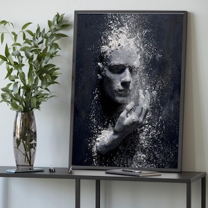 Könnte beinhalten: Gerahmtes Kunstwerk mit einem grauen, geformten Gesicht mit ausgestreckter Hand. Weiße Partikel scheinen von Kopf und Hand vor einem dunklen Hintergrund zu fallen. Das Kunstwerk steht auf einem dunkelgrauen Tisch mit einer Vase mit Grün.