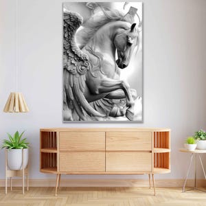 May include: A black and white canvas print of a sculpted Pegasus, a mythical winged horse. The artwork depicts the horse rearing up, showcasing detailed wings and flowing mane. The print is displayed above a wooden cabinet.