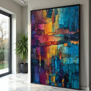 Könnte beinhalten: Großformatiges, gerahmtes abstraktes Kunstwerk mit strukturierter Oberfläche. Das Kunstwerk zeigt eine lebendige Mischung aus Farben, darunter Blau, Orange, Gelb und Lila, wodurch eine visuell auffällige Darstellung entsteht. Das Werk ist in einem schwarzen Rahmen gefasst.