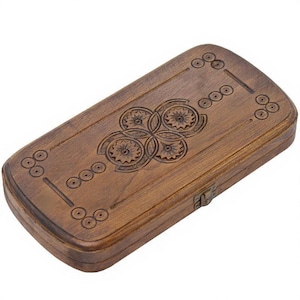 Puede incluir: Un tablero de backgammon rectangular de madera con un acabado marrón oscuro. La parte superior del tablero presenta diseños florales y circulares tallados. Un cierre de metal asegura el tablero.