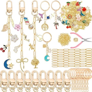 May include: A collection of gold-colored keychains with various charms, including a crescent moon, flowers, and a tree of life. Additional components include key rings, clasps, and jewelry-making tools. The charms are in various colors.