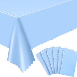 May include: A pale blue tablecloth with a scalloped edge is shown, alongside a stack of matching placemats. The tablecloth is draped, highlighting its texture and design. The placemats feature a decorative border.