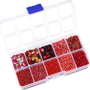 May include: A clear plastic organizer box with a blue clasp, filled with various red and pink beads, sequins, and seed beads. The compartments contain different shapes and sizes, perfect for crafting and jewelry making.