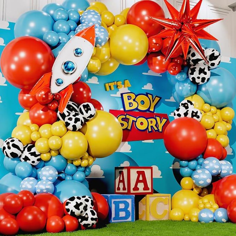 May include: A vibrant balloon display featuring a rocket, a red star, and the text "It's a Boy Story." The balloons are red, yellow, blue, and white with cow print patterns. Wooden blocks spell "ABC."