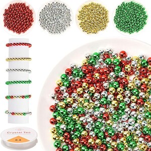 May include: An assortment of colorful beads in red, silver, gold, and green. Several bracelets made of the beads are displayed on a white cylinder. A spool of clear elastic string is also visible. Ideal for jewelry making and crafting.