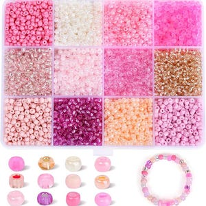 May include: A clear plastic organizer filled with various shades of pink, white, and gold beads. The beads are small and round, perfect for jewelry making. A completed bracelet with pink beads is also shown.