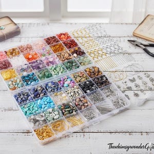 May include: A clear plastic organizer filled with colorful gemstone chips, jewelry findings, and tools. The compartments hold various shades of stones, including pink, green, blue, and brown. Additional findings include gold and silver-toned hoops, clasps, and pins.