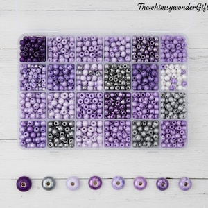 May include: A clear plastic organizer filled with various shades of purple beads. The beads are arranged in small compartments, with a selection of individual beads displayed below. The text "ThewhimsywonderGifts" is in the top right corner.